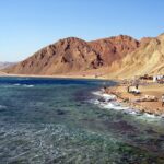 The Blue Hole beach: Bedouin cafés at the foot of ocher mountains, a few cars, rough sea in the foreground
