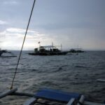 Three dive bancas moored on Monad Shoal under a gray early-morning sky, seen from the deck of another boat