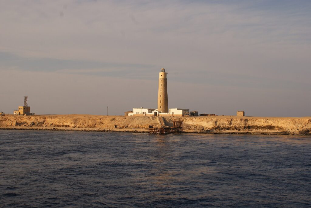 The Big Brother lighthouse and its white buildings on the desert islet, a rusty jetty in the foreground, in golden evening light