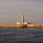 The Big Brother lighthouse and its white buildings on the desert islet, a rusty jetty in the foreground, in golden evening light