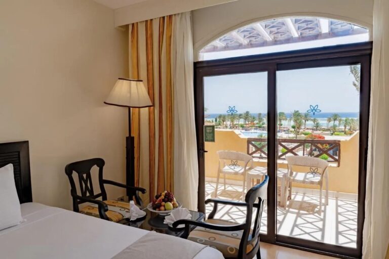 A room with two dark wood armchairs, opening onto a balcony facing the pool and the sea