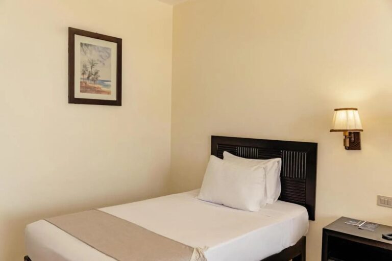 A single bed with a dark wood headboard, under a watercolor of palm trees