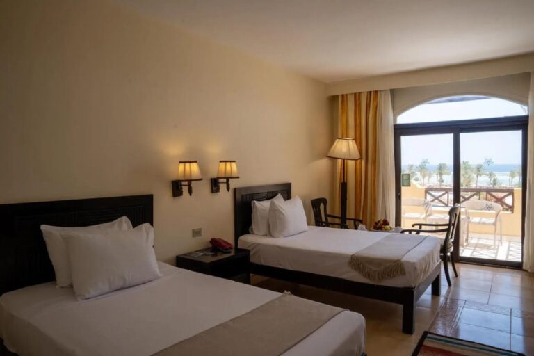 A twin room opening onto a balcony, with a view of the palm trees and the sea