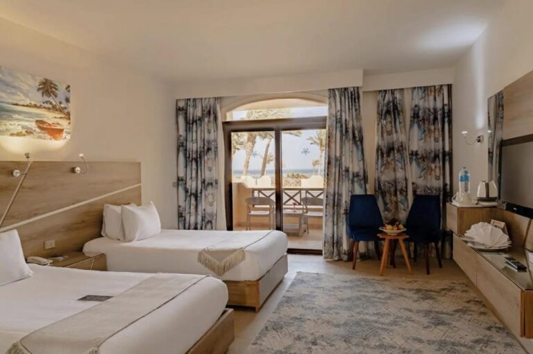 A twin room with two blue armchairs and a glass door onto the balcony