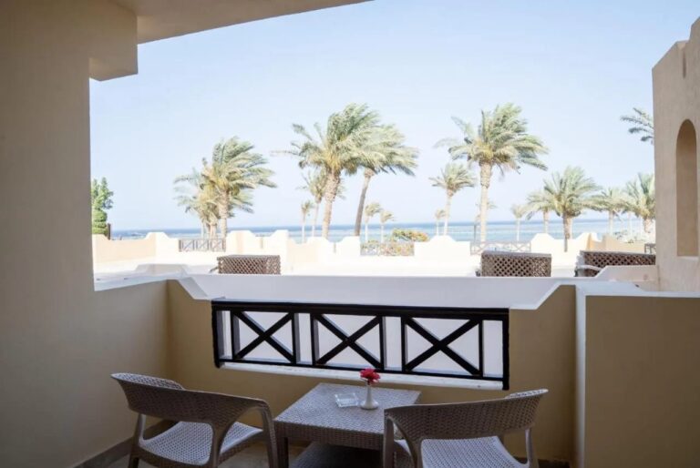 A balcony with two chairs and a small table, facing the palm trees and the sea