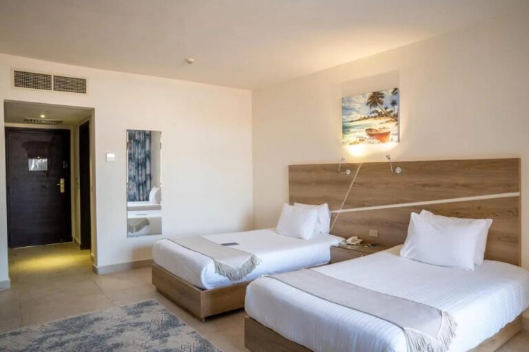 A twin room with a light wood headboard and a beach painting