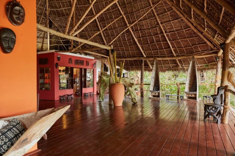 A large open space under a thatched roof, with a wooden floor and African masks