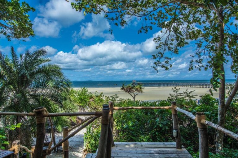 View from a wooden deck over a wide sandy beach and a long jetty