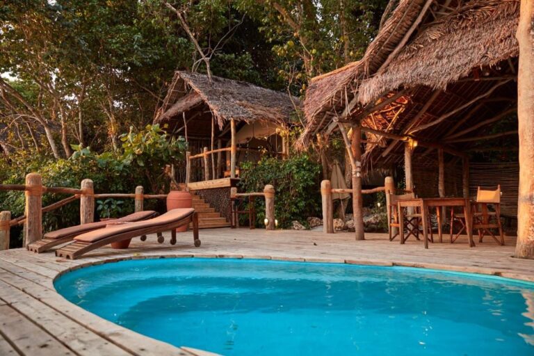 A plunge pool on a wooden deck, with two sun loungers and a table under a thatched roof
