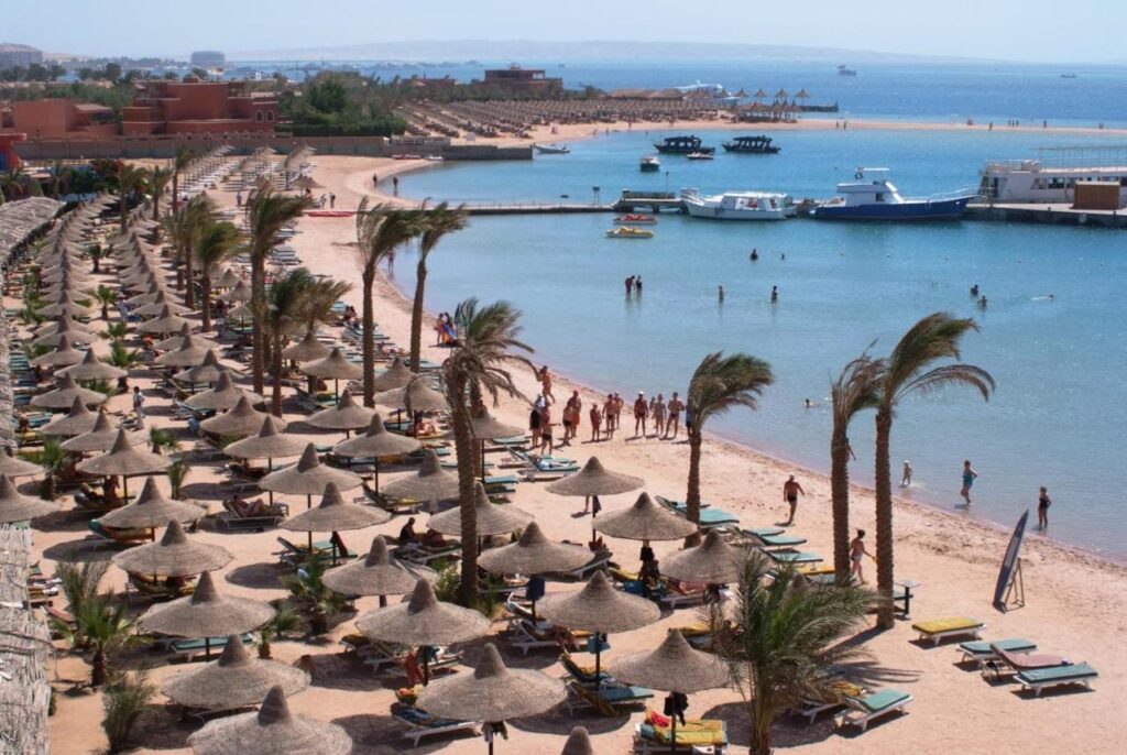 The beach at Giftun Azur Resort, its straw parasols and palm trees, with a jetty and boats in the background