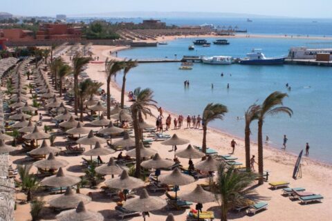 The beach at Giftun Azur Resort, its straw parasols and palm trees, with a jetty and boats in the background