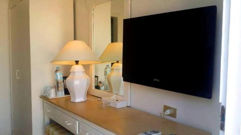 A dresser with a white lamp, a mirror and a wall-mounted TV