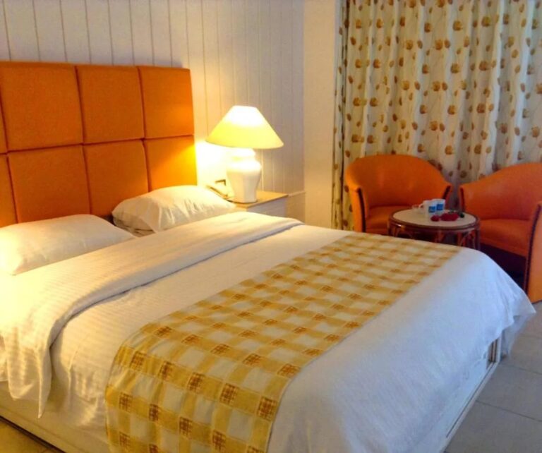 A double bed with an orange headboard, two orange armchairs and a small round table