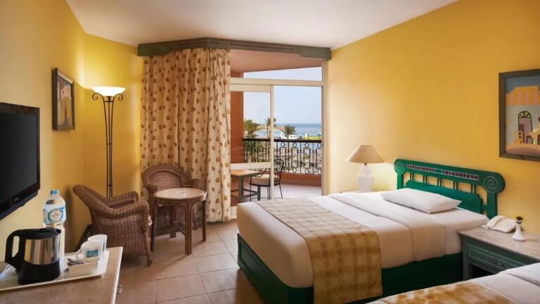 A room with yellow walls, two beds and a balcony facing the sea