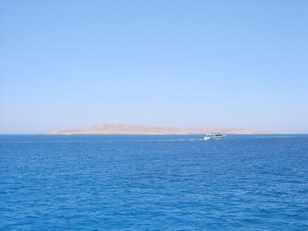 The flat, desert island of Giftun Soraya seen from the sea, a white dive boat passing in front