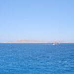 The flat, desert island of Giftun Soraya seen from the sea, a white dive boat passing in front