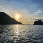 Cocos Island backlit at sunset, with a liveaboard at anchor on the right and a calm sea