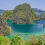 Looking down on a turquoise cove hemmed in by vegetated limestone peaks, a few bangkas moored below and hills on the horizon.