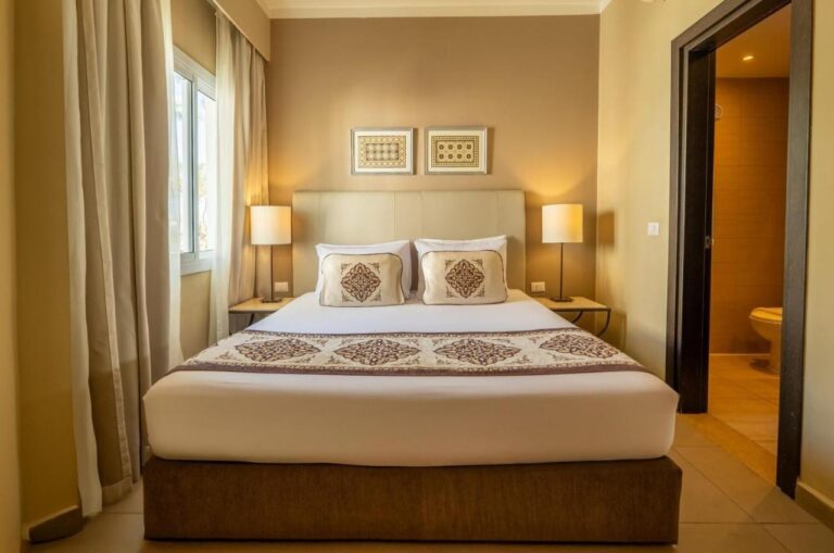 A room with a double bed between two lamps, and the door open onto the bathroom