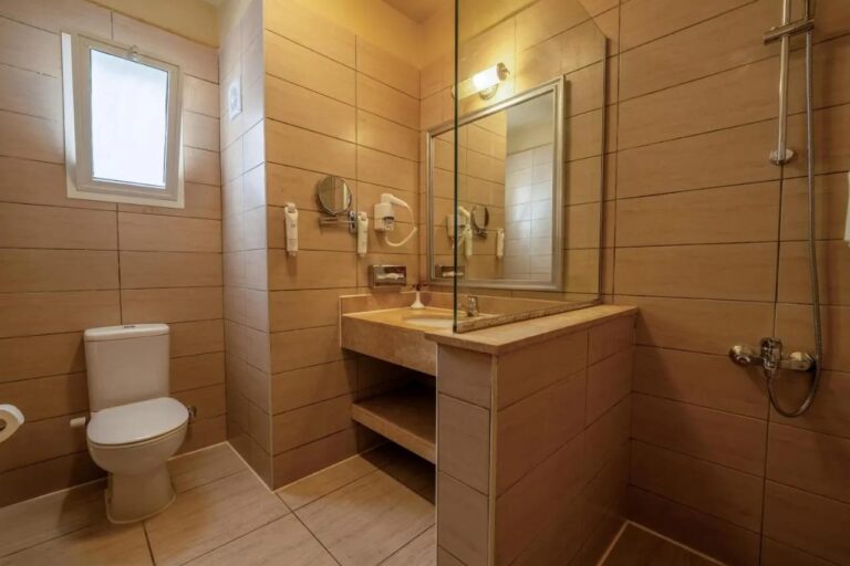 A bathroom with a small window, a basin and a shower behind a glass panel