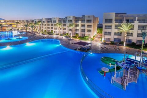 The lit pools of JAZ Soma Beach at nightfall, between the buildings and the palm trees