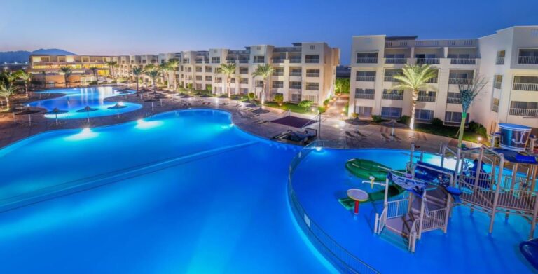 The lit pools of JAZ Soma Beach at nightfall, between the buildings and the palm trees