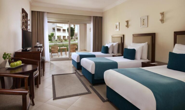 A room with three beds and a round table, opening onto a terrace and the garden