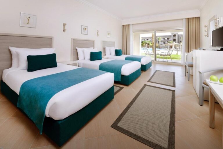 A room with three beds and light furniture, opening onto a terrace facing the pool