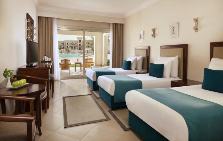 A room with three beds and dark wood furniture, with a terrace facing the pool