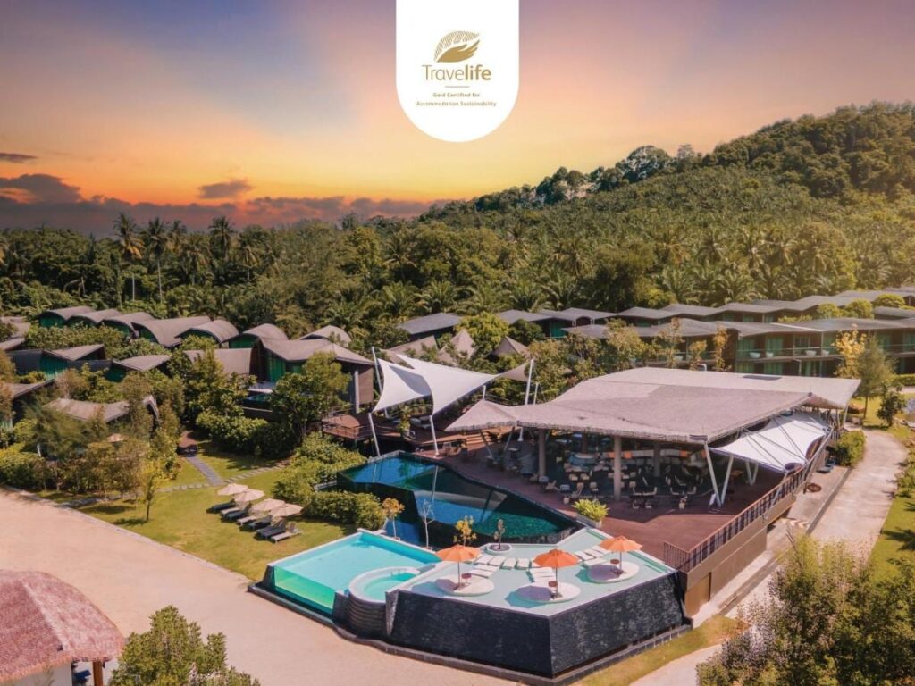 Aerial view of Kalima Resort Khao Lak at sunset, its pools and curved roofs at the foot of a wooded hill