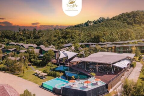 Aerial view of Kalima Resort Khao Lak at sunset, its pools and curved roofs at the foot of a wooded hill