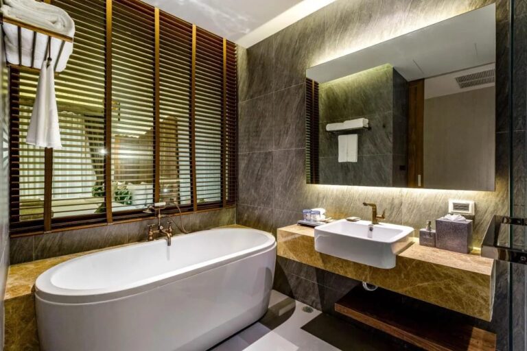 An oval bathtub in front of wooden shutters, next to a basin