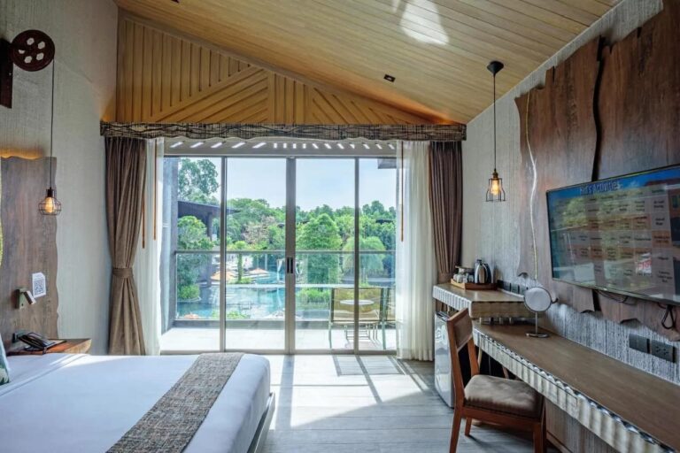 A room under a wooden ceiling, opening onto a balcony that overlooks the pool