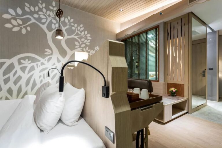A bed against a wall painted with a white tree, with a reading light