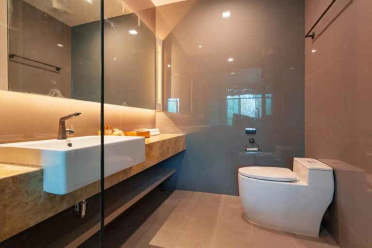 A bathroom with a basin on a marble counter, a lit mirror and a toilet