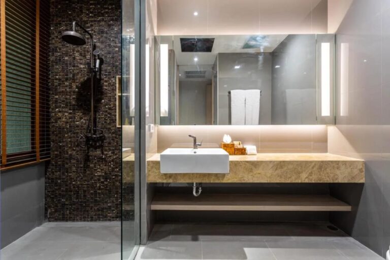 A shower against a dark mosaic wall, next to a basin under a lit mirror