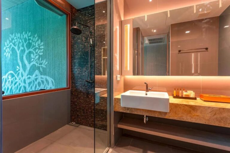 A shower behind a glass panel, near a window decorated with a tree