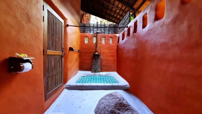 A semi-open bathroom with orange walls and a shower on a turquoise mosaic floor