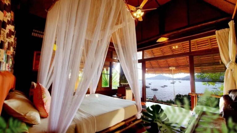 A room with a bed under a mosquito net, opening onto the bay and the boats