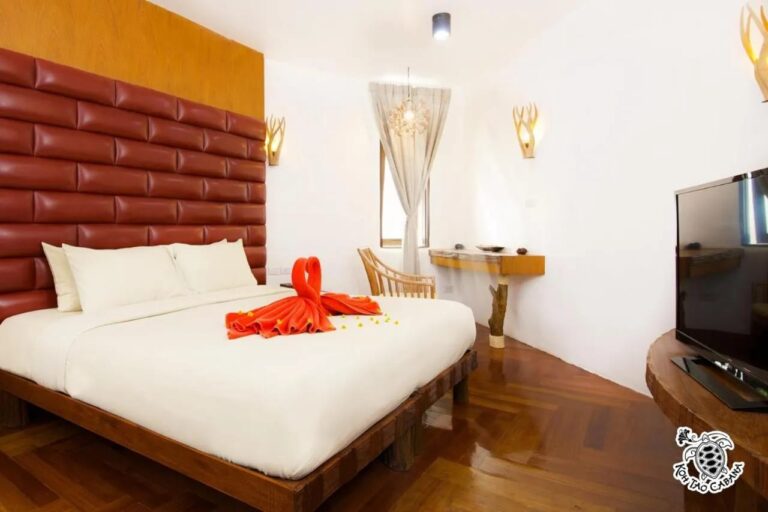 A white room at Koh Tao Cabana, with a double bed, a red padded headboard and a TV