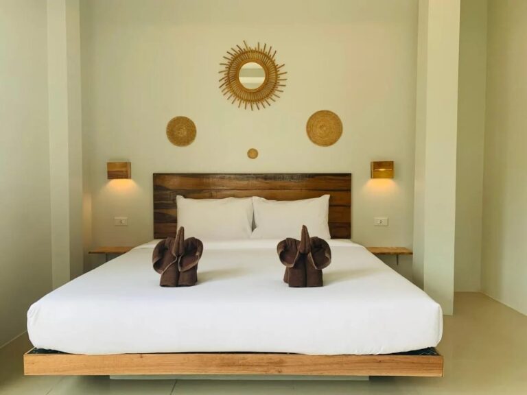 A double bed with a wooden headboard, towel elephants and a rattan sunburst mirror