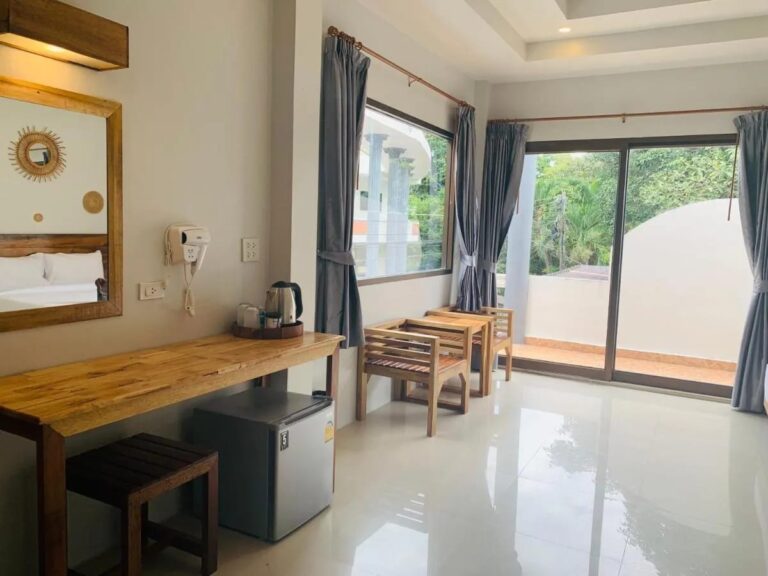 A wooden desk with a kettle and a small fridge, near the picture window onto the balcony