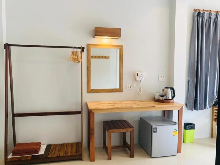 A wooden clothes rack, a mirror and a desk with a kettle above a small fridge
