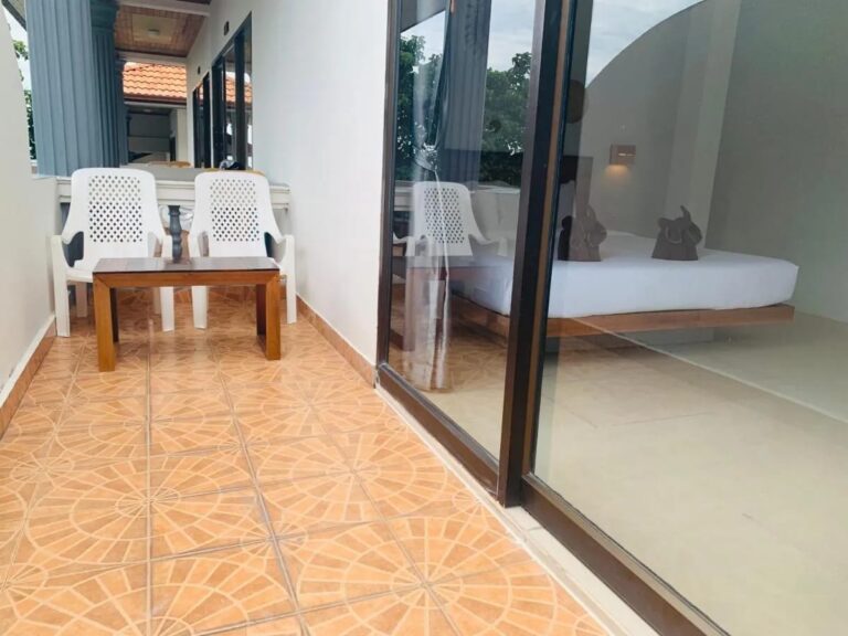 A tiled balcony with two white chairs and a coffee table, in front of a room's picture window