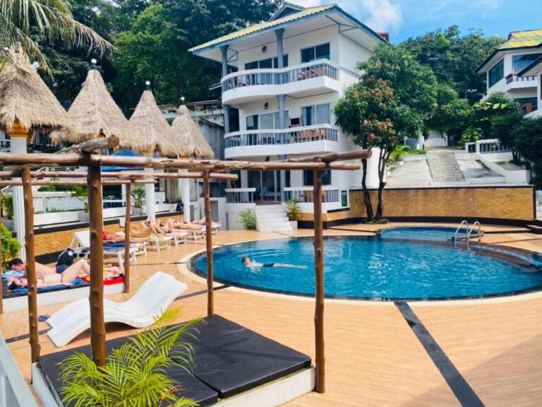 The pool at Koh Tao Heritage, its sun loungers and straw parasols, in front of a building with balconies