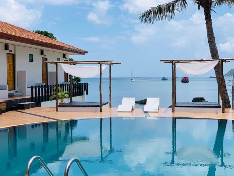 The pool facing the sea, with two daybeds under a pergola and white sun loungers
