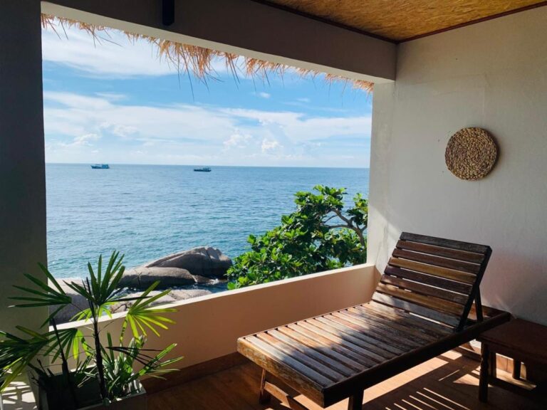 A covered terrace with a wooden lounge chair, facing the sea and the rocks