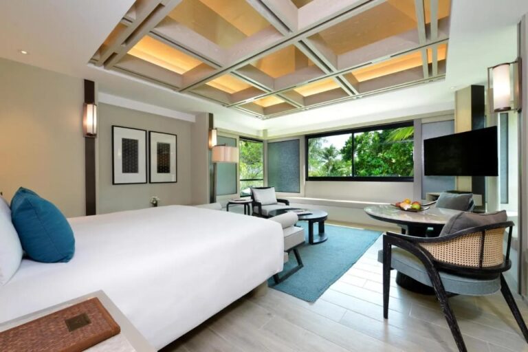 A double room with a coffered ceiling, a sitting area and a window onto the palm trees