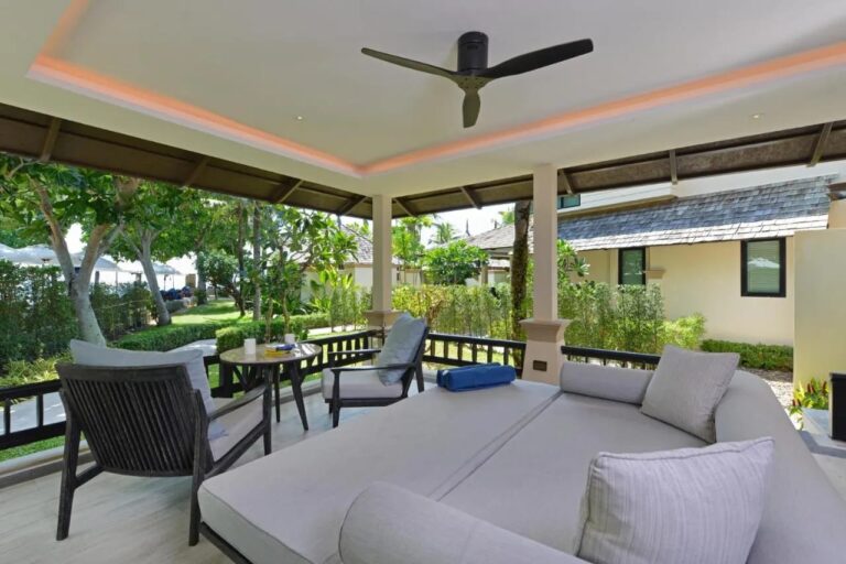 A covered terrace with a large daybed, two armchairs and a ceiling fan