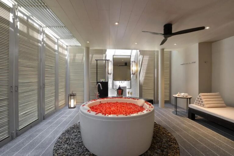 A bathroom with shutters, a round bathtub in the center and a bench seat